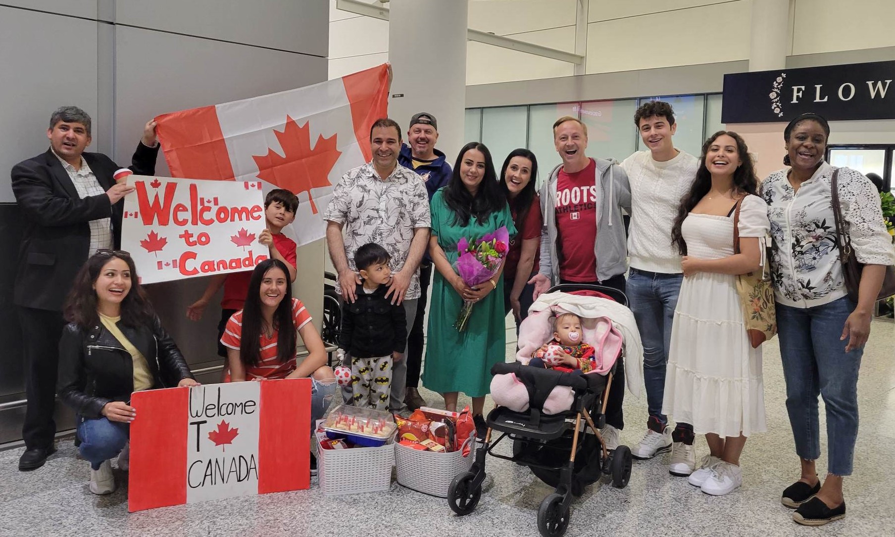 Shawn, Obed, and other supporters welcoming a just-arrived refugee family with Canadian flags, flowers, and food baskets, at the airport.