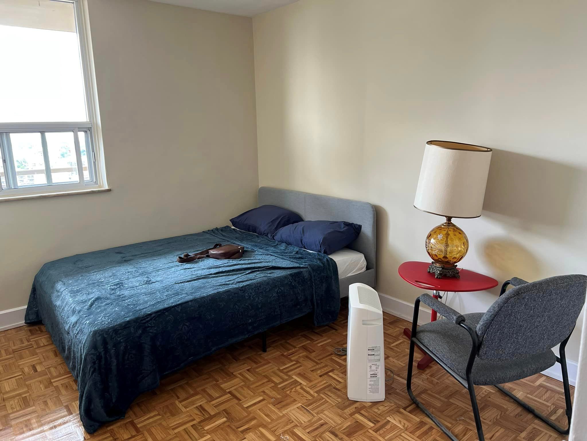 A bedroom with a single bed, side table, lamp, and chair